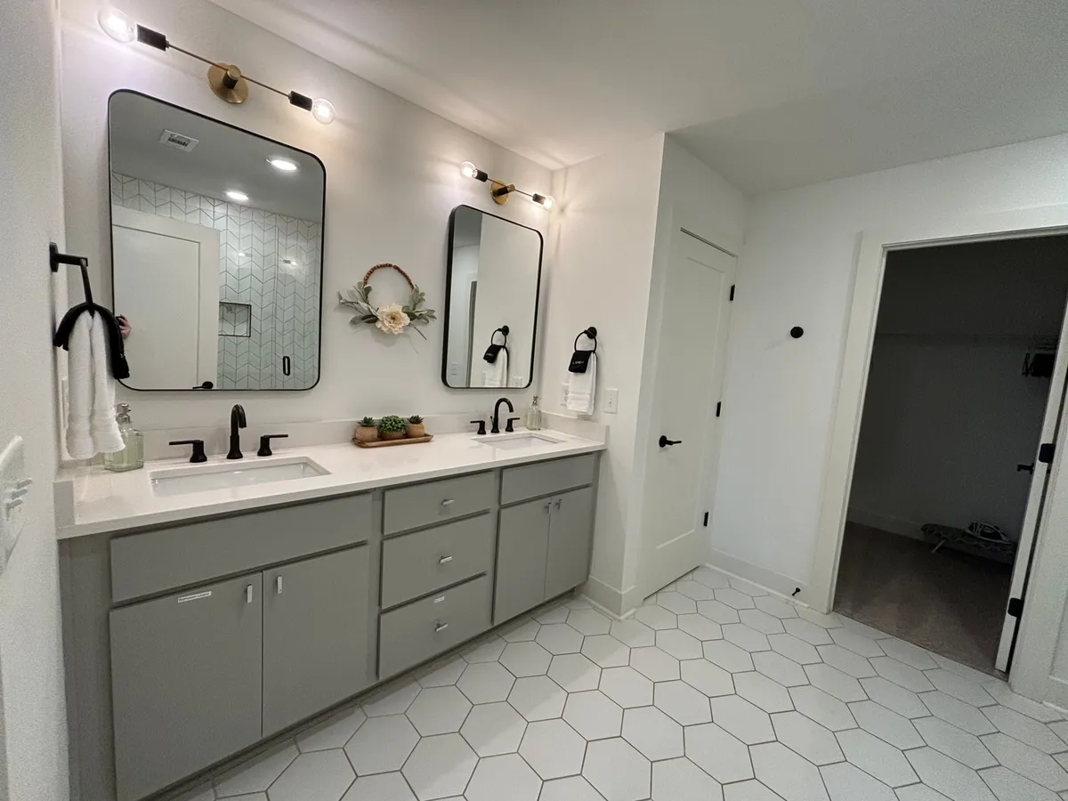 A contemporary bathroom with dual mirrors, modern fixtures, a hexagonal tile floor, and a decorative plant arrangement, providing a fresh and stylish environment for daily routines.