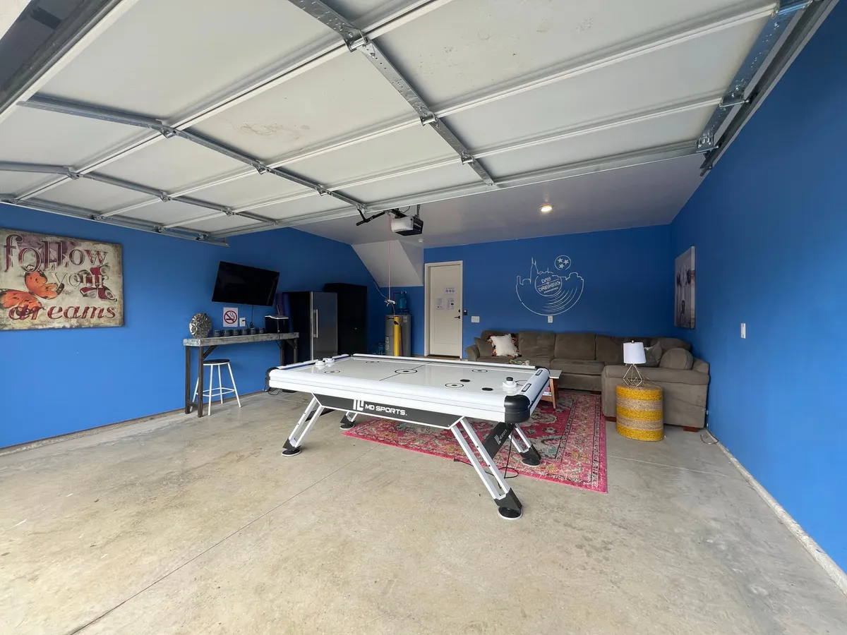A lively scene with an air hockey table as the focal point, accompanied by a cozy sofa, colorful rug, blue walls, and wall art. The space exudes a playful, relaxed atmosphere ideal for game nights and casual hangouts.