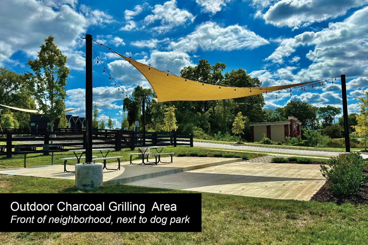 An inviting outdoor communal space with a grilling area, shade sail, picnic tables, a landscaped pathway, and a dog park. The area is designed for socializing, relaxing, and casual outdoor gatherings, highlighting the communal aspects of the property.