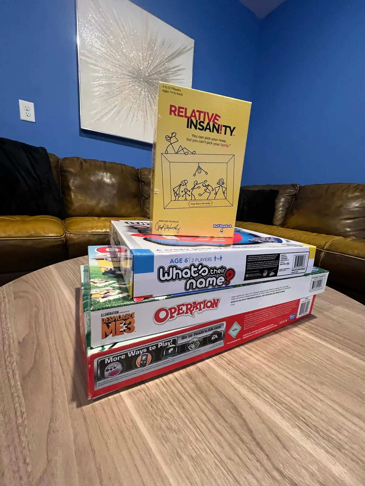 A close-up of a collection of board games set on a table, with modern wall art and a comfy brown couch in the background. The playful mood is set for memorable game nights and laughter-filled gatherings.