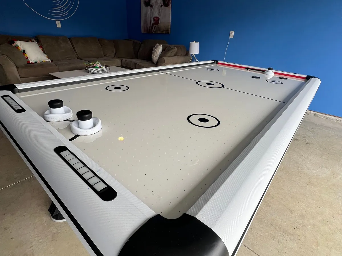 A vibrant entertainment space with an air hockey table, a comfortable sofa adorned with colorful pillows, and a stylish lamp. The scene feels lively and ready for spontaneous fun or relaxed hangouts.
