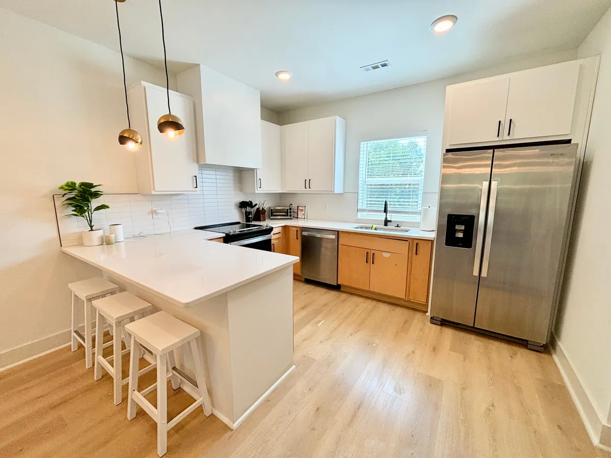 A modern chef’s kitchen featuring a central island with bar stools, gleaming stainless steel appliances, and abundant natural light streaming through a window. The space offers plenty of room for cooking, dining, and mingling.